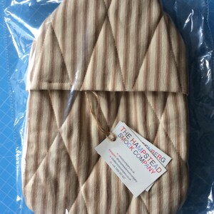 Pode incluir: Uma capa acolchoada para garrafa de &aacute;gua quente em listras marrons e brancas com um padr&atilde;o de losangos. A capa tem uma etiqueta anexada com o texto "The Hampstead Smock Company" e informa&ccedil;&otilde;es de contato.