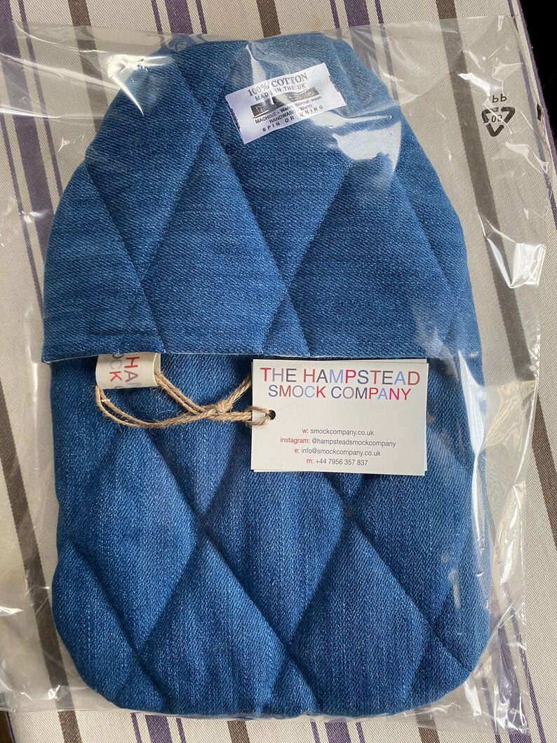 Pode incluir: Uma capa para garrafa de &aacute;gua quente de ganga azul com um padr&atilde;o acolchoado de losangos. A capa est&aacute; embalada num saco de pl&aacute;stico transparente com um r&oacute;tulo que diz "The Hampstead Smock Company" e inclui informa&ccedil;&otilde;es de contacto.