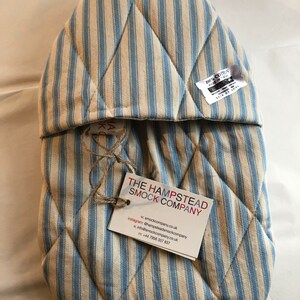 Pode incluir: Luva de forno acolchoada em azul e branco listrado com uma etiqueta que diz "The Hampstead Smock Company" e inclui informa&ccedil;&otilde;es de contato. 100% algod&atilde;o, feito no Reino Unido.