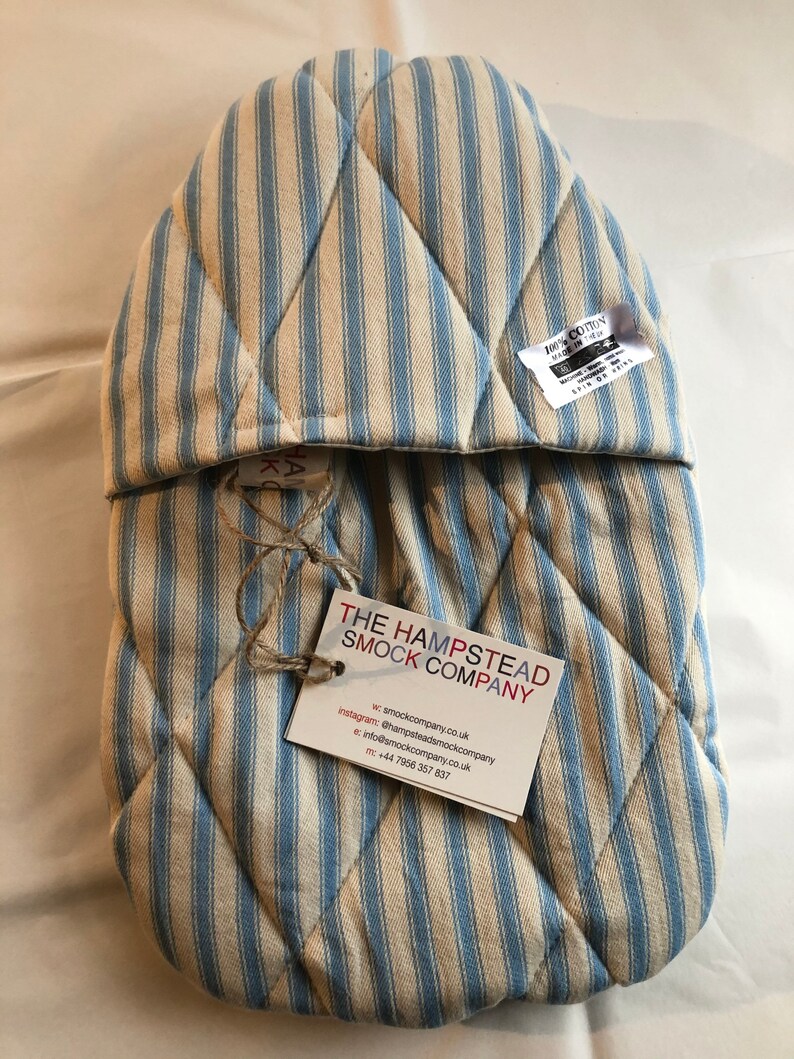 Pode incluir: Luva de forno acolchoada em azul e branco listrado com uma etiqueta que diz "The Hampstead Smock Company" e inclui informa&ccedil;&otilde;es de contato. 100% algod&atilde;o, feito no Reino Unido.