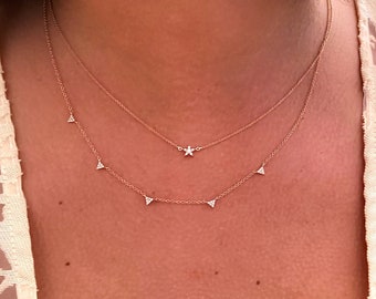 May include: A woman wearing a white lace top with a delicate gold necklace featuring a star charm and a row of small triangle charms.