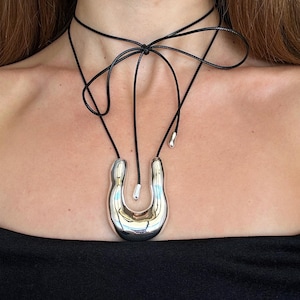 May include: A silver abstract pendant necklace with a black cord. The cord is tied in a bow at the back of the neck.