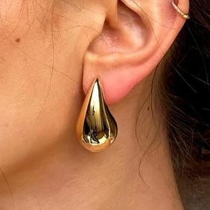 May include: Gold teardrop shaped earrings. The earrings are a simple, modern design.