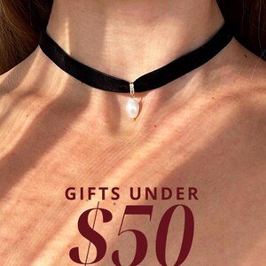 May include: A black velvet choker necklace with a single white pearl pendant. The text "GIFTS UNDER $50 SHOP NOW" is displayed below the necklace.