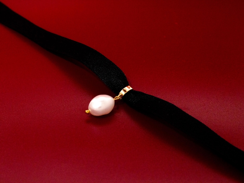 May include: A black velvet choker necklace with a single white pearl pendant.