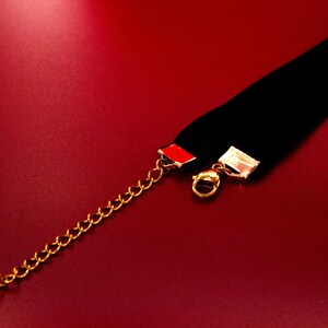 May include: A black velvet choker necklace with a gold chain and clasp. The choker has a red accent on the back.