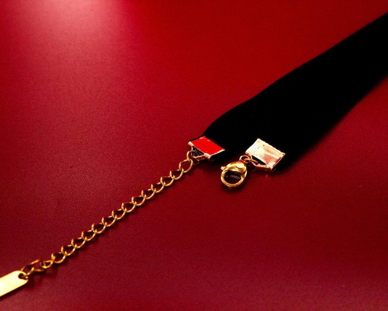 May include: A black velvet choker necklace with a gold chain and clasp. The choker has a red accent on the back.