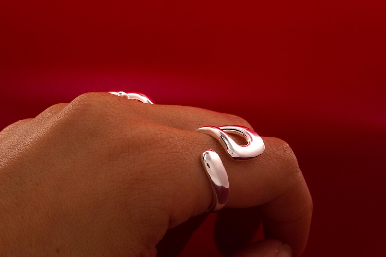 May include: A silver ring with a unique, abstract design. The ring is worn on a person's finger.