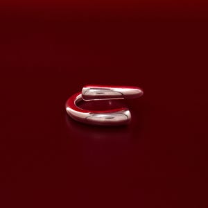 May include: A silver ring with a unique, curved design. The ring is made of two pieces of metal that are joined together to form a continuous loop.