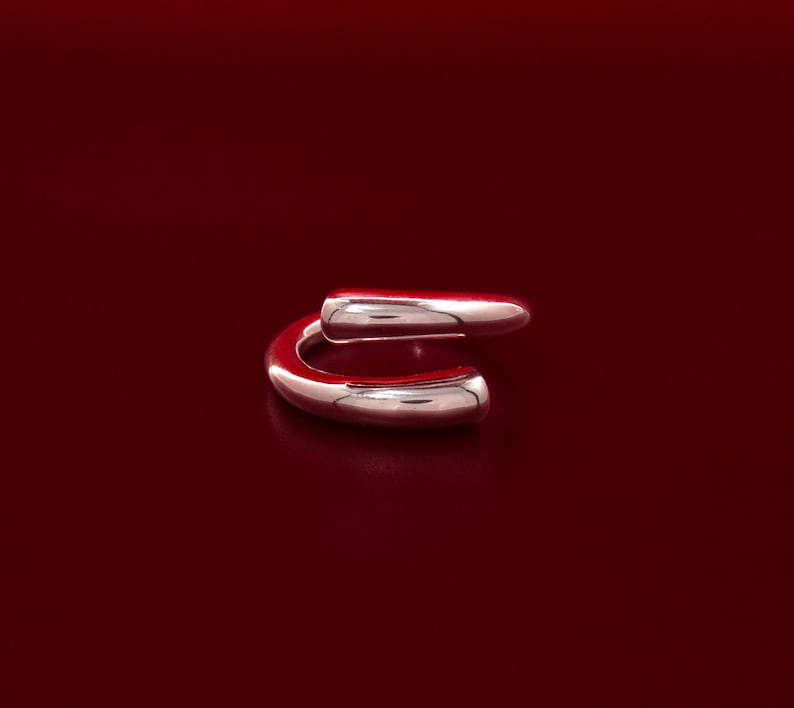 May include: A silver ring with a unique, curved design. The ring is made of two pieces of metal that are joined together to form a continuous loop.