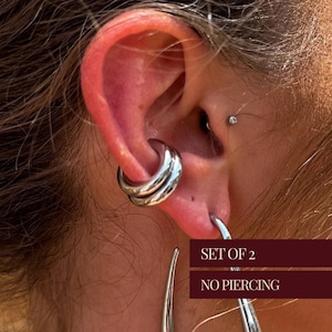 May include: A set of two silver ear cuffs. The cuffs are designed to be worn without piercing. The text "SET OF 2 NO PIERCING" is visible in the image.