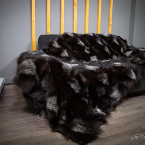 Könnte beinhalten: Eine schwarze und silberne Fuchspelzdecke, die über ein dunkelgraues Sofa gelegt ist. Die Decke hat eine luxuriöse und weiche Textur.