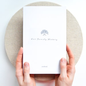 May include: A white notebook with the text "Our Family History" and a small tree illustration. The notebook is being held by two hands.
