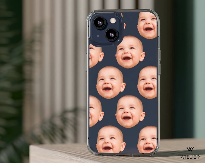 May include: A clear phone case with a repeating pattern of smiling babies' faces on a dark blue background. The case is designed for an iPhone 14 Pro.