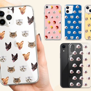 May include: A clear phone case with a repeating pattern of cat and dog faces. The case is shown on a hand holding it. There are other phone cases in the background with different patterns.