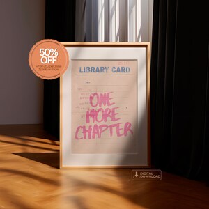 K&ouml;nnte beinhalten: Ein gerahmter Druck mit einem Vintage-Bibliothekskartendesign. Der Text "ONE MORE CHAPTER" ist in Pink auf die Karte geschrieben. Der Druck ist in einem hellen Holzrahmen und liegt auf einem Holzboden.