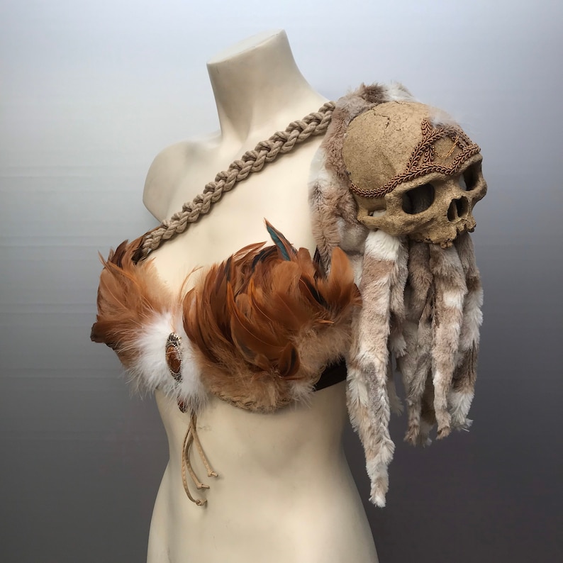 May include: A brown and white feathered costume piece with a skull and fur accents. The skull is decorated with a gold-colored band.