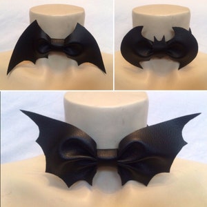 May include: Three black leather bow ties shaped like bat wings. The bow ties are on mannequins with light brown skin.