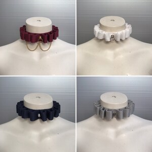 Könnte beinhalten: Vier verschiedene Stoffkragen mit gekräuselten Kanten. Die Kragen sind in Burgunderrot, Weiß, Marineblau und Grau. Jeder Kragen hat einen kleinen Metallring in der Mitte.