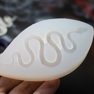 May include: A white silicone mold shaped like a leaf with a snake design inside. The mold is designed for making resin crafts.