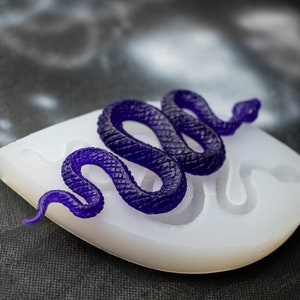 May include: A purple resin snake casting in a white silicone mold. The snake is coiled and has a textured surface.