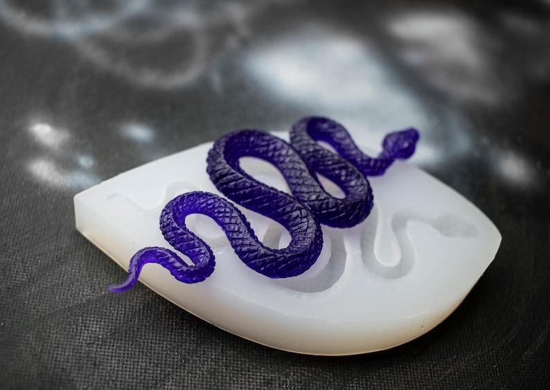 May include: A purple resin snake casting in a white silicone mold. The snake is coiled and has a textured surface.