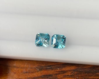 May include: Two square-shaped, light blue gemstones with a faceted cut.