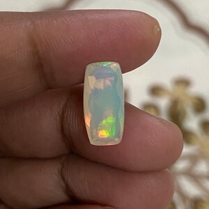 Peut inclure: Une pierre précieuse d'opale blanche de forme rectangulaire avec des reflets irisés verts et orange.