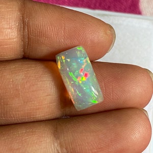 May include: A white opal gemstone with a rectangular shape and a rainbow of colors, including green, yellow, red, and orange.