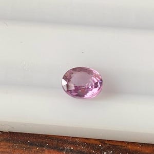Puede incluir: Una piedra preciosa ovalada de color rosa claro con facetas.