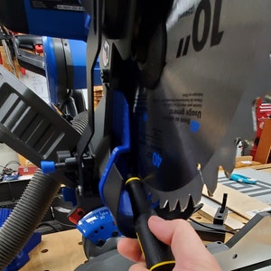 May include: A close-up of a black and yellow screwdriver being used to tighten a screw on a blue and black miter saw. The saw blade is visible and has the text "10" and "40" printed on it. The saw is labeled "DELTA".