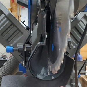 May include: Close-up of a black and blue miter saw with a black dust collection shroud. The saw blade is visible and the saw is partially assembled.