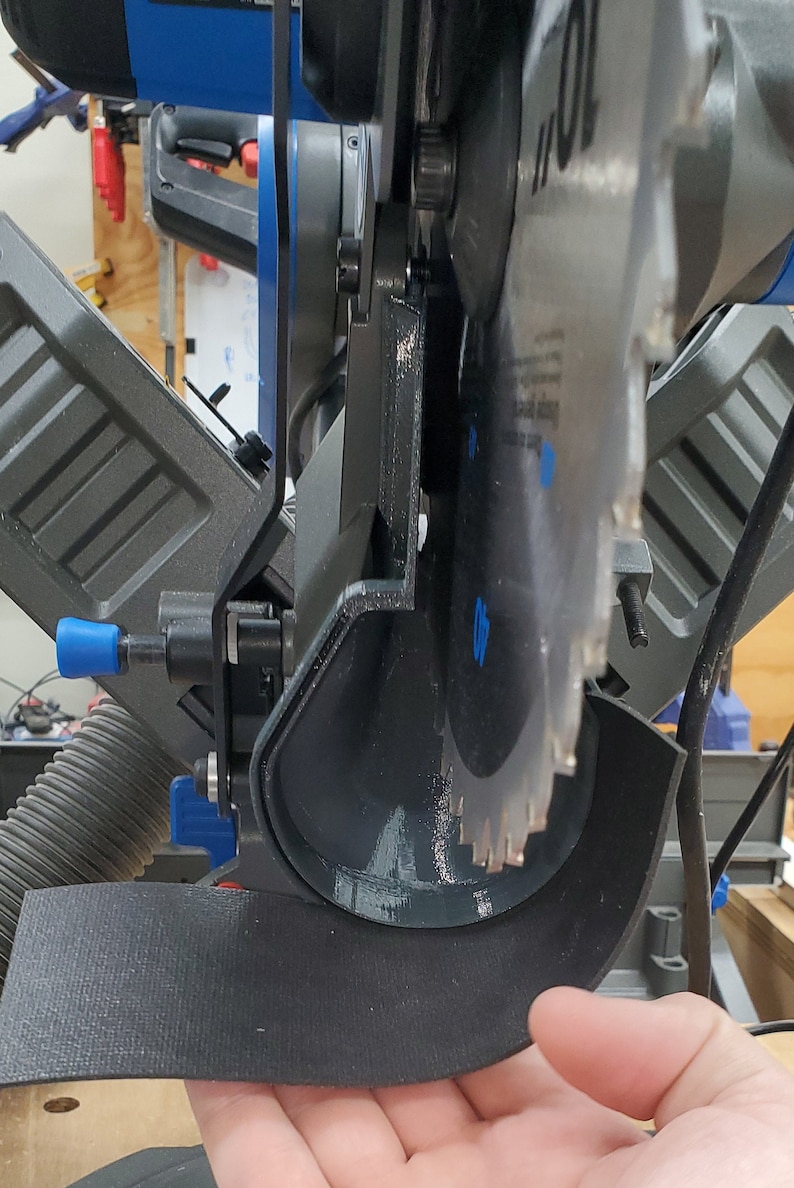 May include: Close-up of a black and blue miter saw with a black dust collection shroud. The saw blade is visible and the saw is partially assembled.