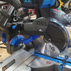 May include: A black and blue Delta power miter saw with a clear plastic guard. The saw blade is visible and has the text "10" printed on it.