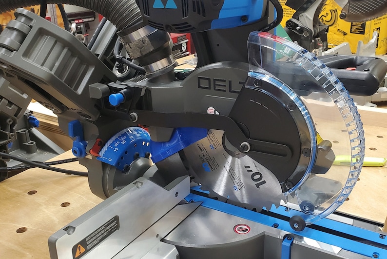 May include: A black and blue Delta power miter saw with a clear plastic guard. The saw blade is visible and has the text "10" printed on it.