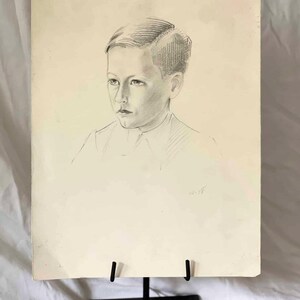 May include: Pencil portrait of a young person on aged paper, displayed on a black metal easel. The portrait features a detailed rendering of the subject's face and hair, with shading and lines. The artwork is signed and dated.