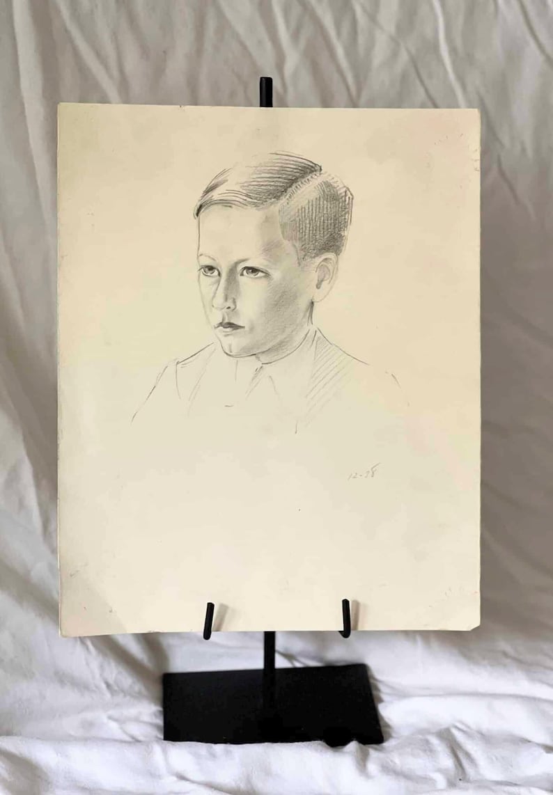 May include: Pencil portrait of a young person on aged paper, displayed on a black metal easel. The portrait features a detailed rendering of the subject's face and hair, with shading and lines. The artwork is signed and dated.