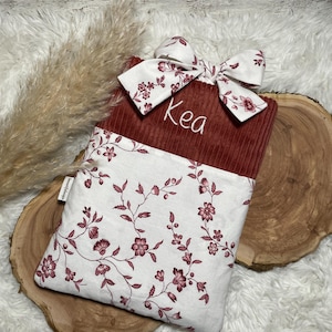 Könnte beinhalten: Ein Set aus drei Keramikbechern mit einer gesprenkelten, cremefarbenen Glasur. Jeder Becher hat ein anderes handgemaltes Design: ein blaues und grünes Blatt, eine gelbe und orangefarbene Blume und eine rote und rosa Beere. Die Becher haben eine einfache, abgerundete Form.