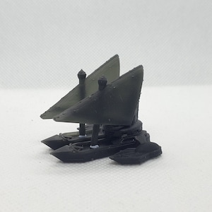 May include: Two miniature black and green sailboats with a pointed bow and a flat bottom. The sailboats have a single mast and a single sail. The sails are made of a translucent material and are partially filled with air. The sailboats are sitting on a white surface.