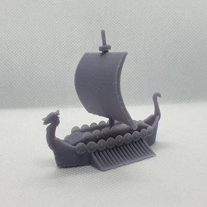 May include: A small, gray, 3D printed model of a Viking ship with a dragon head prow and a single sail. The ship has a row of round shields along the sides.