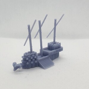 Op de afbeelding: Een grijs 3D-geprint model van een klein, antiek schip met een ramneus en meerdere masten. Het schip heeft een houten dek en een verhoogd platform aan de achterkant.
