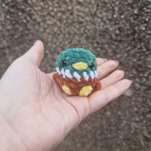 Mini crochet mallard duck plush sitting in palm for size comparison