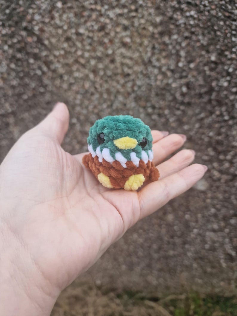 Mini crochet mallard duck plush sitting in palm for size comparison