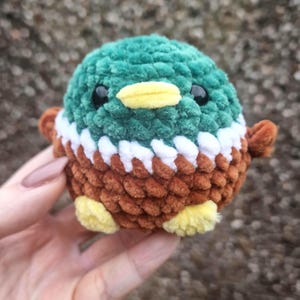 Handmade crochet mallard duck plush toy held in hand showing green head, white collar and brown body