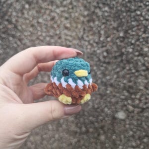 Mini crochet mallard duck plush held in hand against textured background