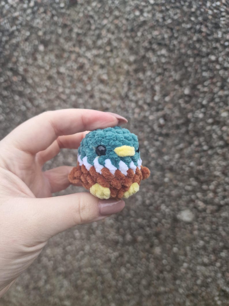 Mini crochet mallard duck plush held in hand against textured background