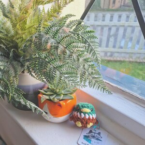 Mini crochet mallard duck plush displayed on windowsill with plant