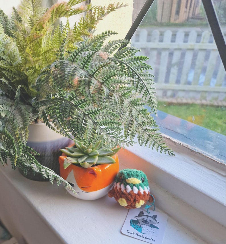 Mini crochet mallard duck plush displayed on windowsill with plant