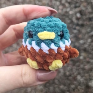 Tiny handmade crochet mallard duck plush held between fingers showing miniature size