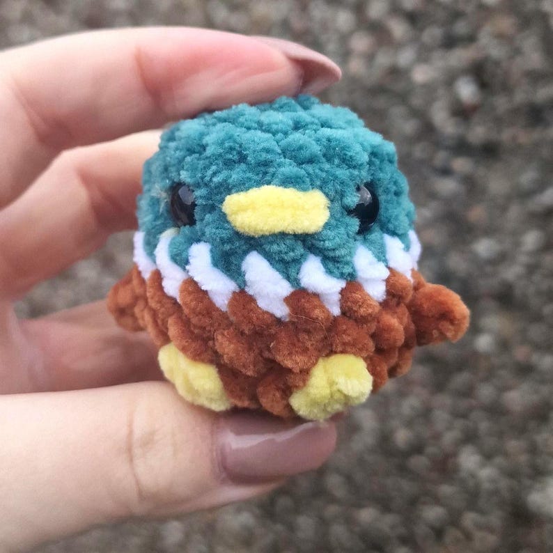Tiny handmade crochet mallard duck plush held between fingers showing miniature size